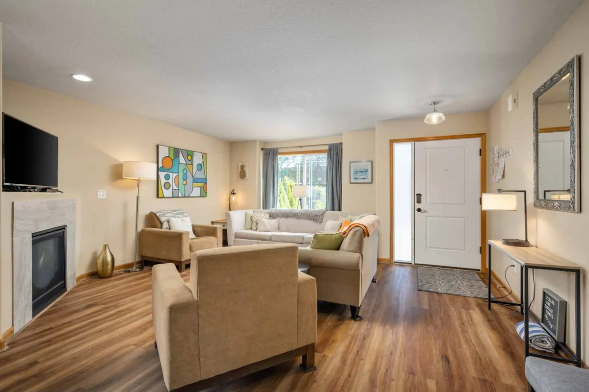 A focus on the living room side, this image highlights a comfortable sofa, a flickering gas fireplace, modern artwork, and a window drawing in abundant natural light. The arrangement sets the scene for socializing, reading, or relaxing.