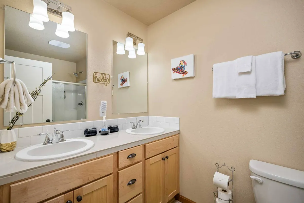 A bright and airy bathroom with a double sink vanity, large mirrors, and tasteful wall art. The space feels fresh and inviting, perfectly suited for morning routines or evening wind-downs, in line with the modern amenities described in the section.