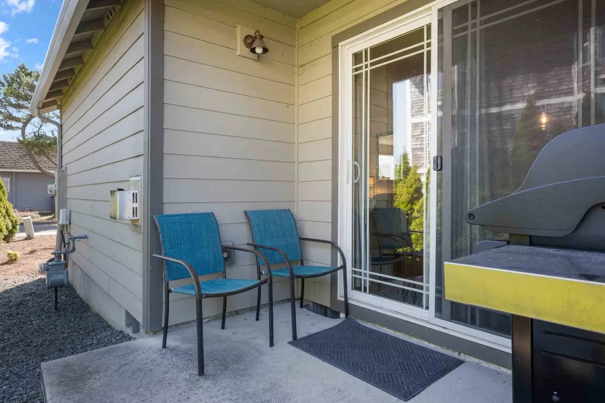 A cozy patio area just outside a sliding glass door, featuring two blue chairs and a grill. The setup invites socializing, barbecuing, and enjoying meals in the fresh air, seamlessly connecting indoor and outdoor living.