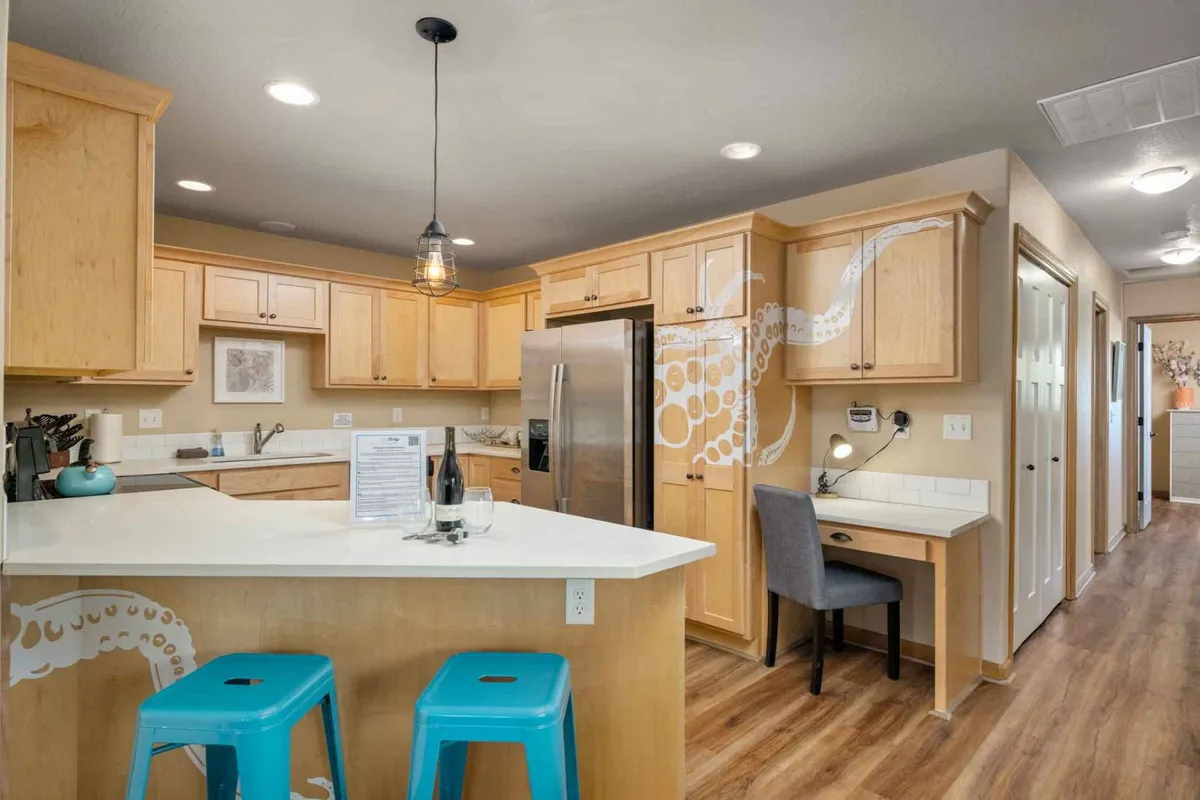 A stylish kitchen interior with a white counter, playful blue stools, a striking octopus mural on the wall, and stainless steel appliances. The space feels open and designed for casual dining and entertaining guests.