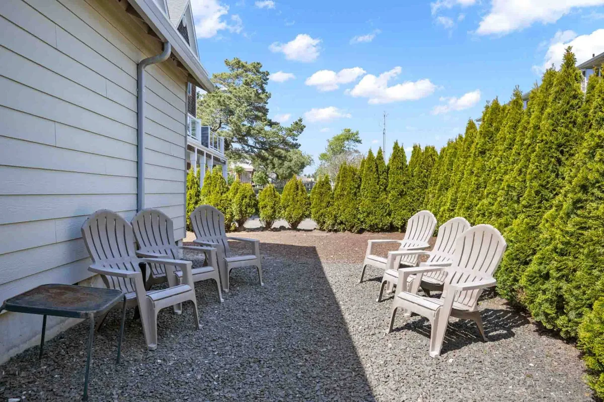 An inviting backyard scene with plastic chairs arranged on a gravel surface, bordered by a well-kept hedge line. The open, spacious area exudes a sense of calm and privacy, perfect for relaxing or socializing outdoors.