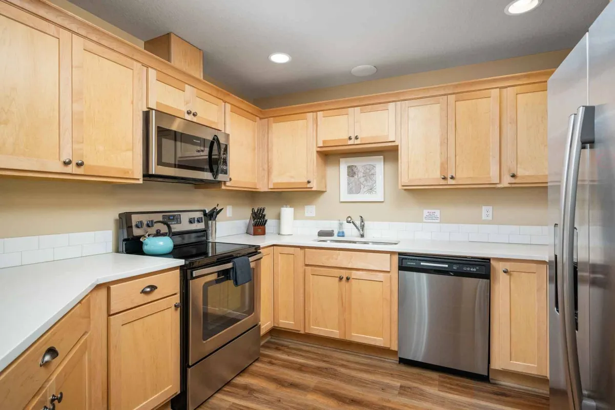 A bright, welcoming kitchen featuring modern appliances, wooden cabinets, a spacious countertop, and a sink. The scene evokes the warmth of family gatherings, meal prep, and shared cooking experiences.