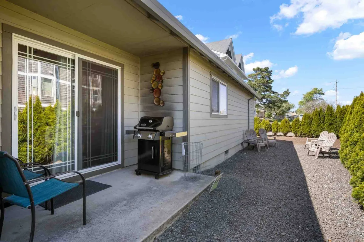 A well-appointed backyard patio with a prominent grill, comfortable outdoor seating, and lush landscaped hedges. The area is set for relaxed barbecues or evening gatherings with friends.